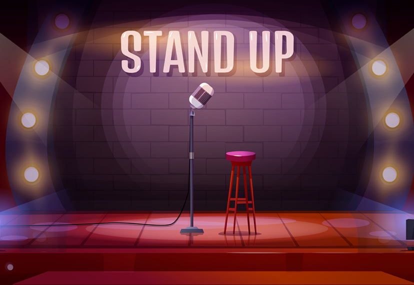 A stand-up microphone is on a stage besides a red stool. The microphone and stool are in front of a black wall that says “stand up” in white bubble letters. The wall was has three bulb lights on each side illuminating the stage.