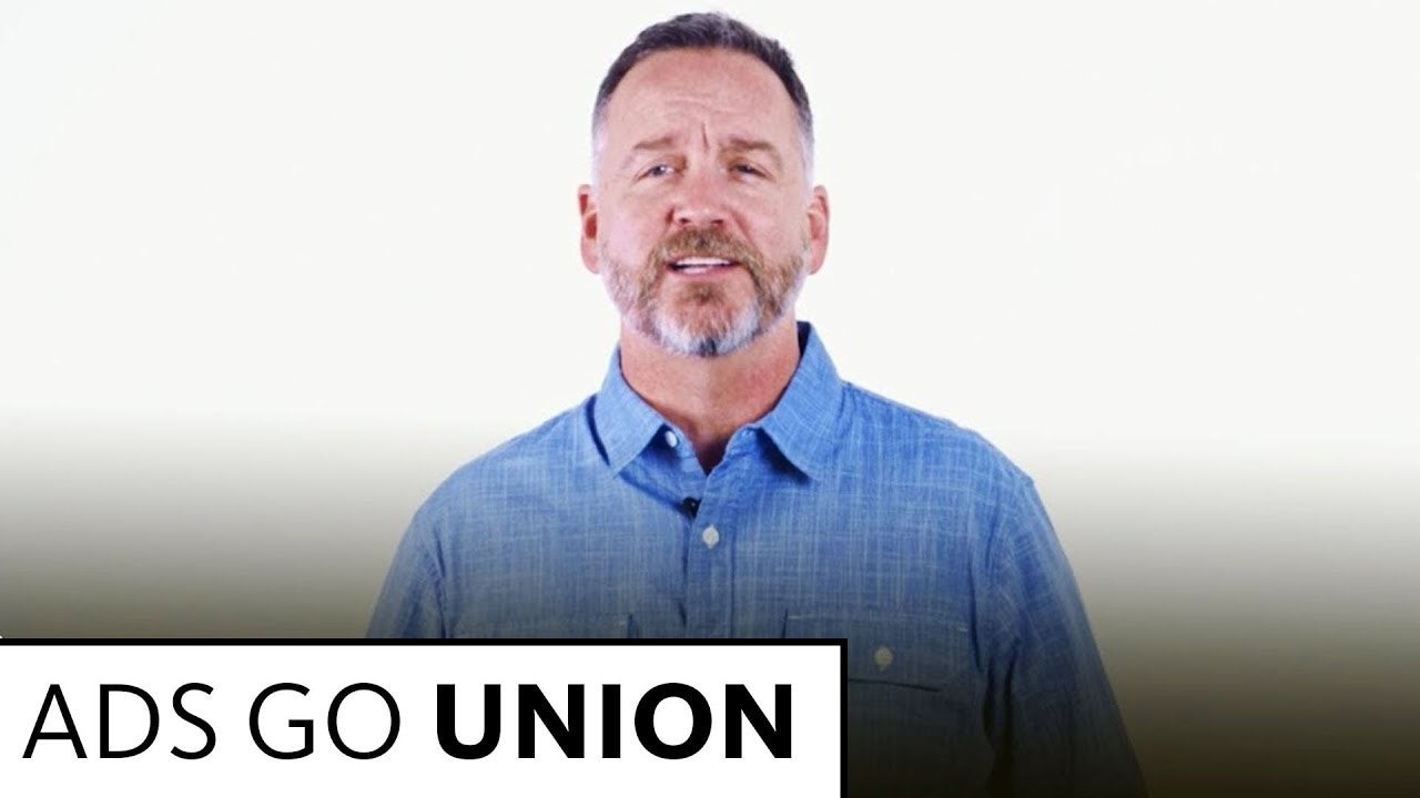 Anderson in light blue button up speaking into camera with a white background