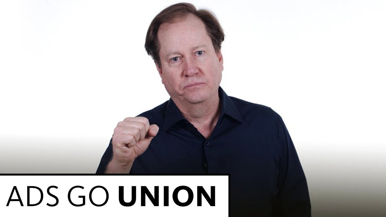 Connor holding right fist in front of him looking directly at camera wearing dark blue button up on a white background