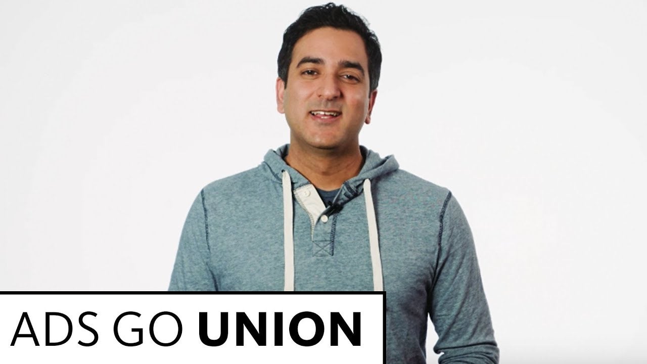 Sharma in teal blue pullover jacket standing in front of white background