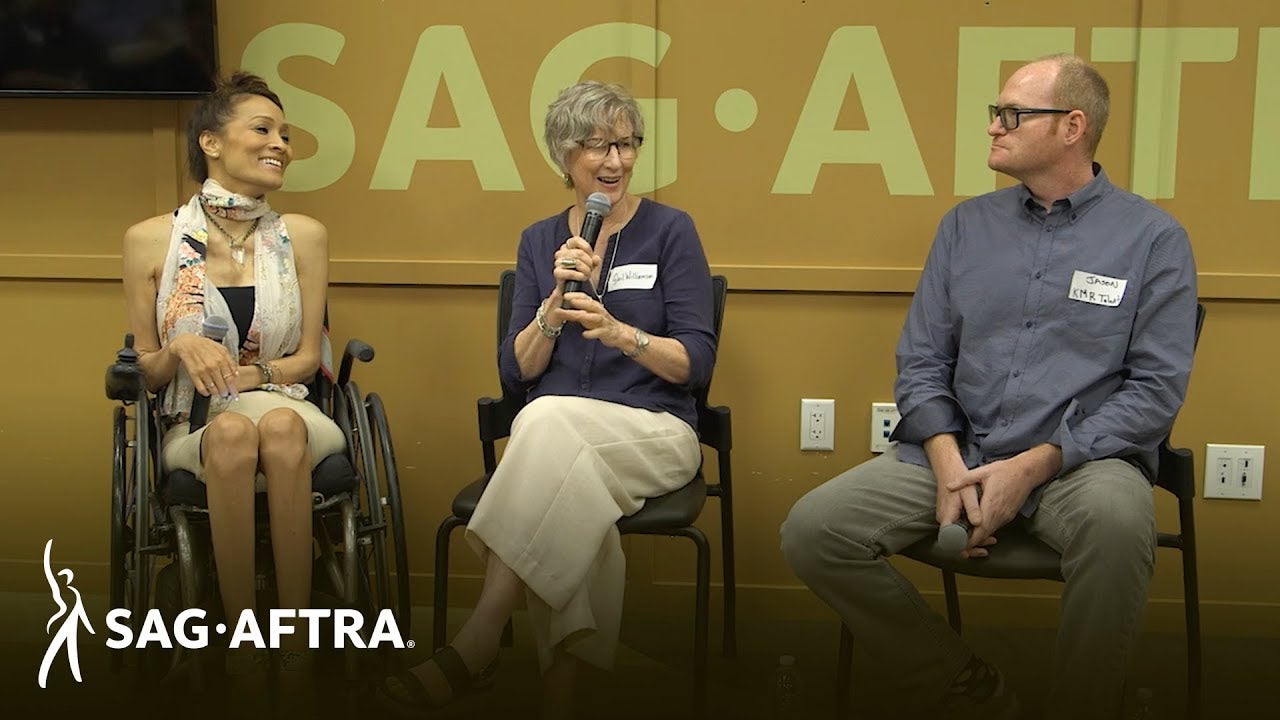 Three panelists siting side by side speaking into a mic and looking at the panelist in the middle. 