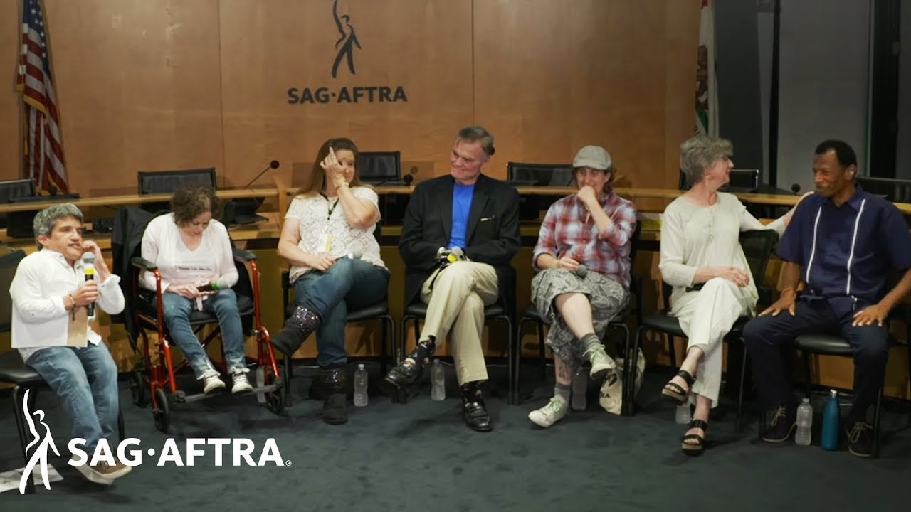 Panelists seated shoulder to shoulder facing audience. L-R: Povinelli, Russo, O'Rourke, Lawson, Goodman, Williamson and Jones