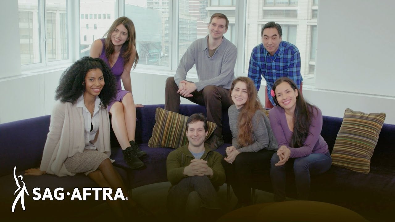 Members sitting on couch cushions, back of couch or in front of couch smiling at camera