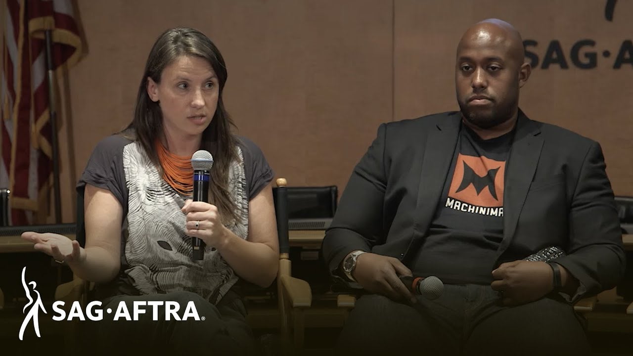 Panelist on left in black and white top speaking into mic with panelist on left in black shirt and black blazer looking out at audience