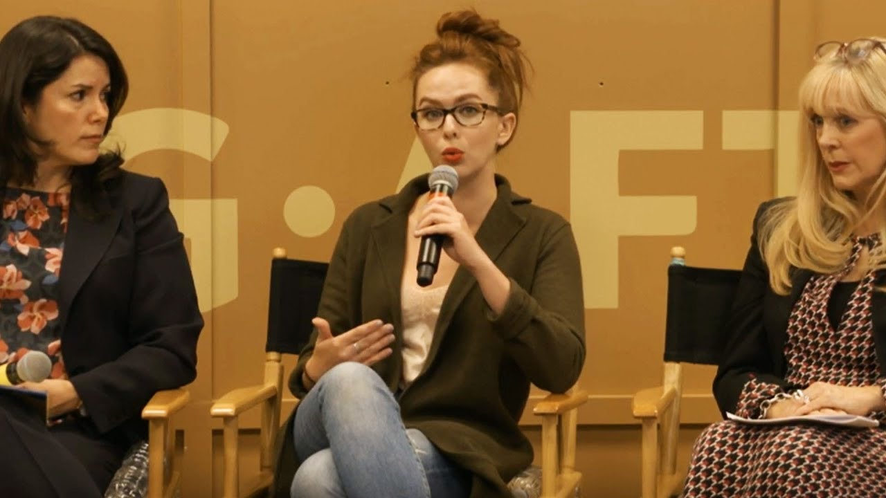 Panelist in middle speaking into microphone with woman on left and right