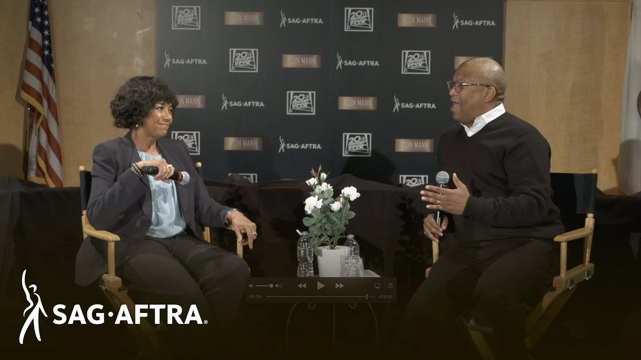 Panelist on left in light top with grey pants and blazer looking over at panelis on right speaking to woman on left wearing a black pullover and black pants