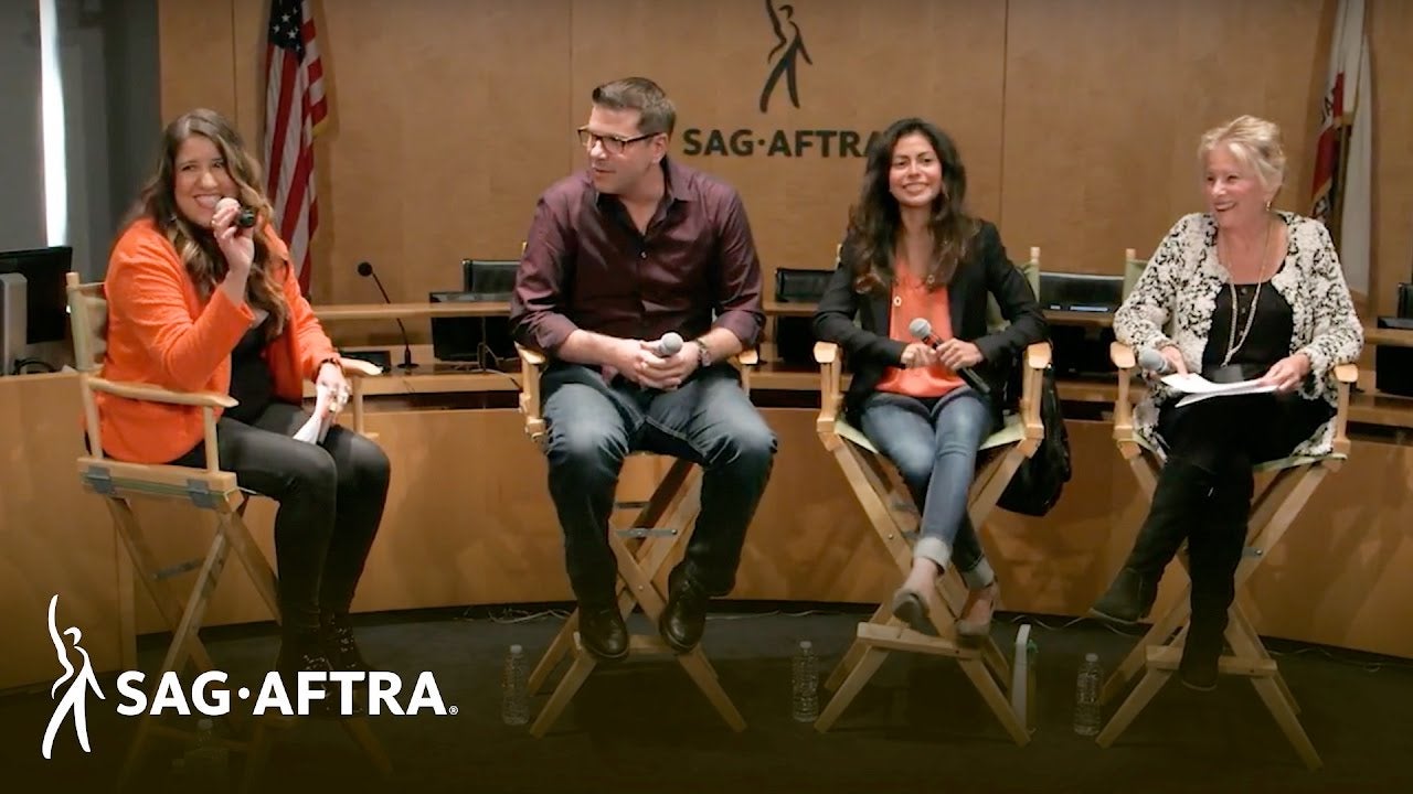 Moderator speaking to audience smiling and three panelists on right looking at moderator