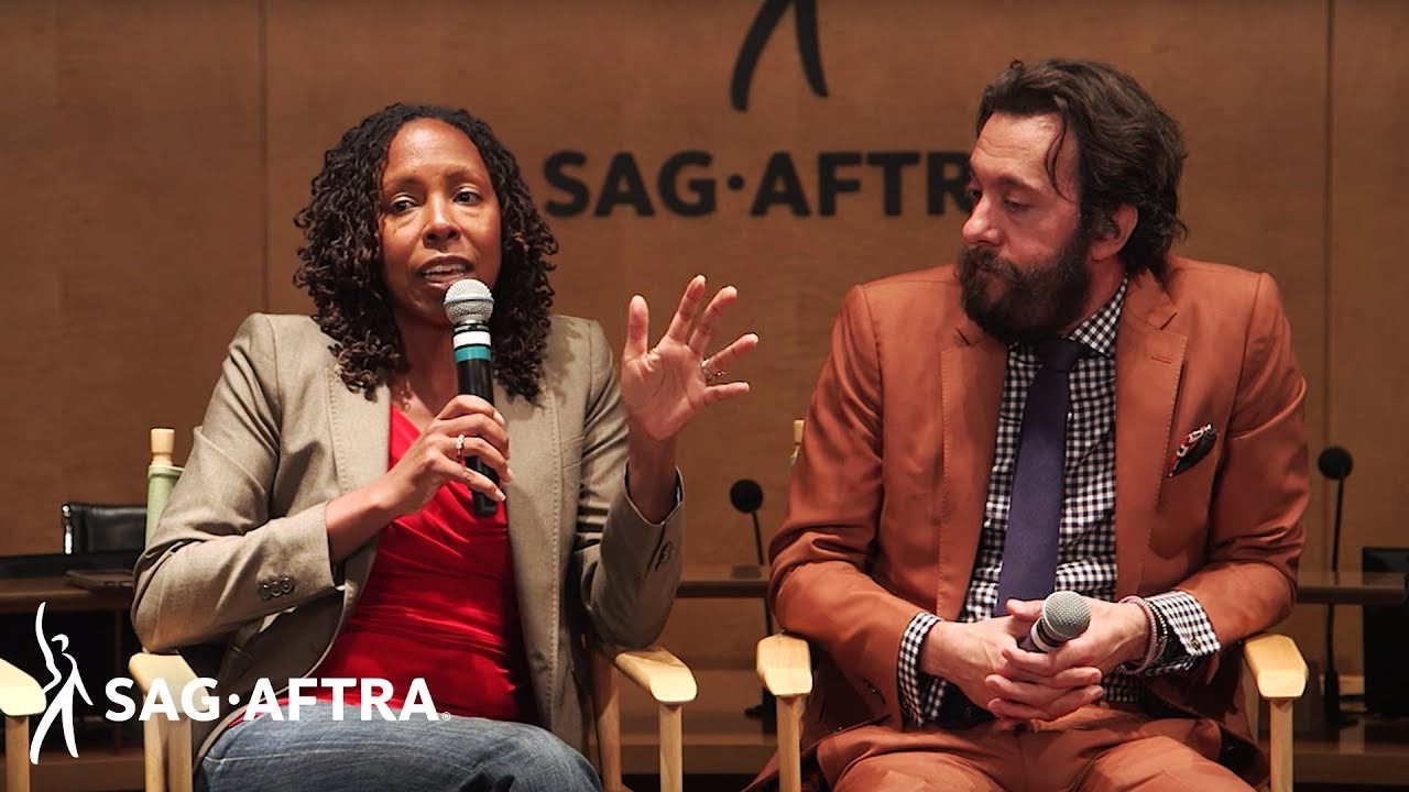 Panelist on left speaking into microphone looking out at audience and panelist on right looking at her speak. 