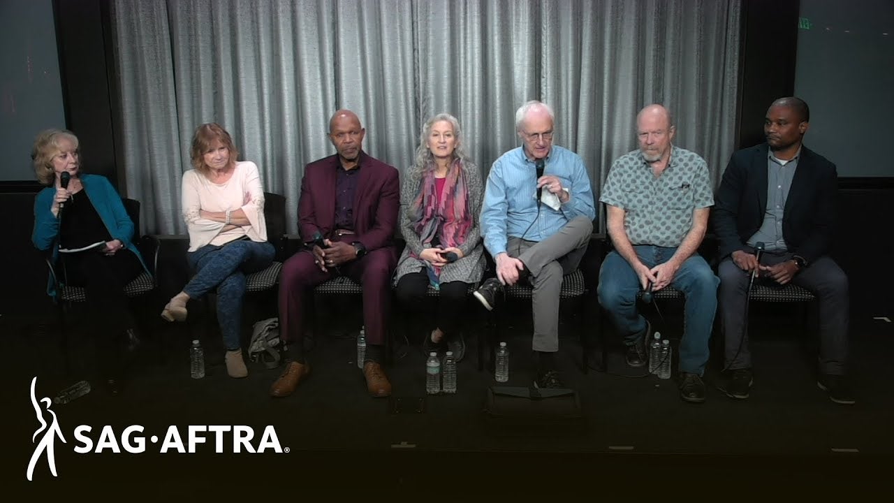 Row of panelists sitting and listening to each other while looking at audience.
