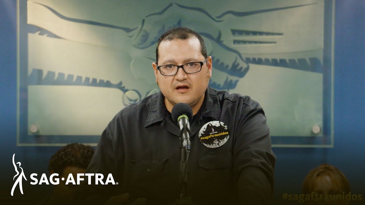 Castillo in black button up speaking into microphone at podium