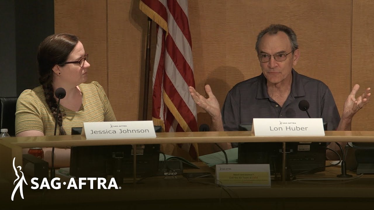 Panelist Johnson on left looking to her left at Huber in a grey collar shirt. Name cards in front on table top