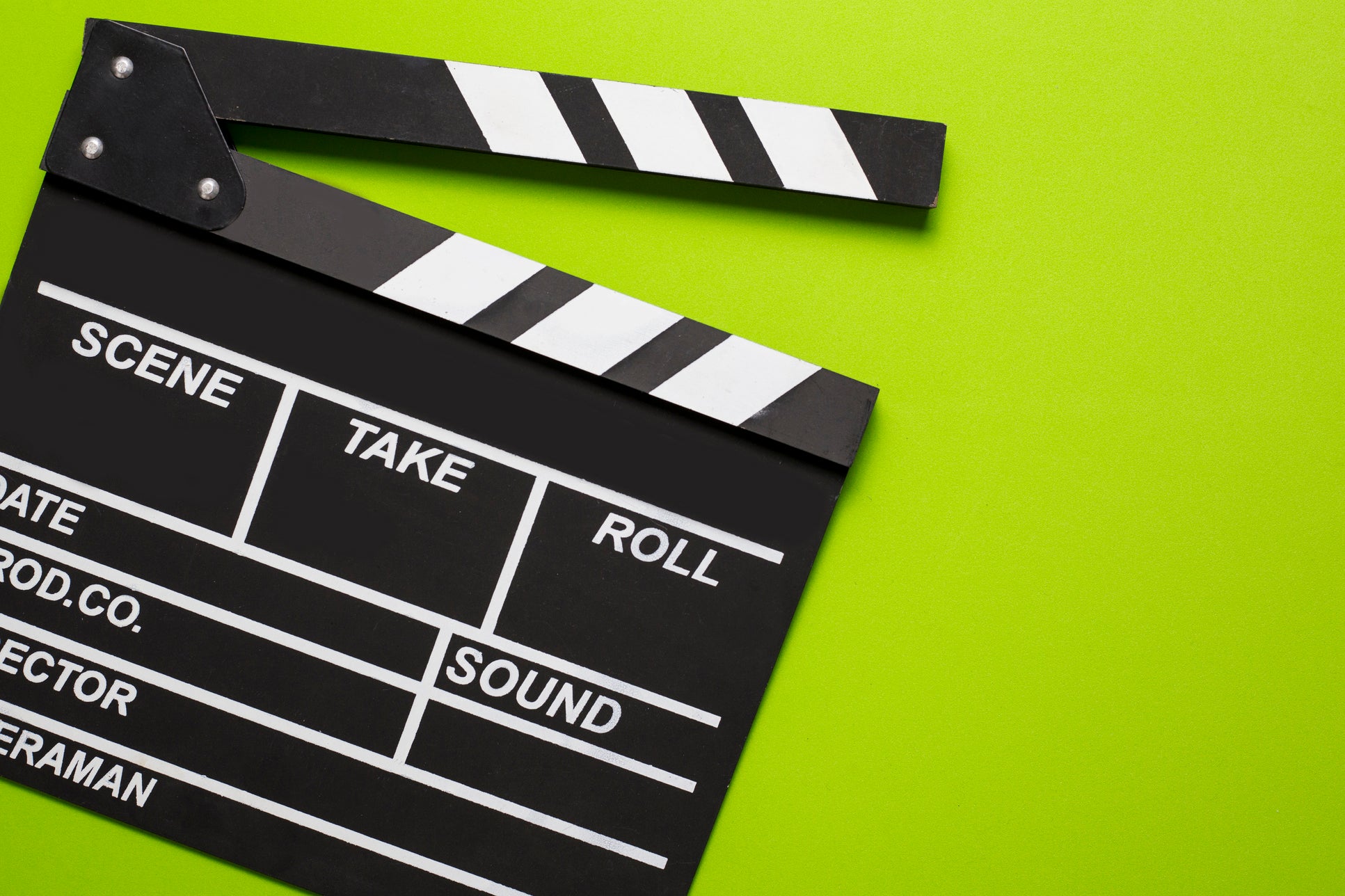 A  black and white clapperboard is placed on a green background. The clapperboard is slightly open and has sections labeled "Scene", "Take", "Roll", "Date", "Prod Co", "Sound", "Director", and "Cameraman."