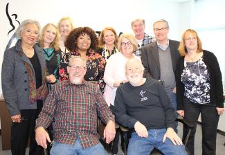 A diverse group of men and women sit with Mark Wenner, front row left, and Bill Wax, front row right. Wenner and Wax are seated. 