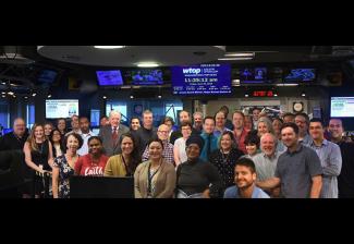 A diverse group of men and women stand in a new newsroom.