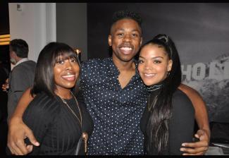 Three African-American young adults at the viewing party. Center figure, male, holds an arm around the women flanking him on either side. 