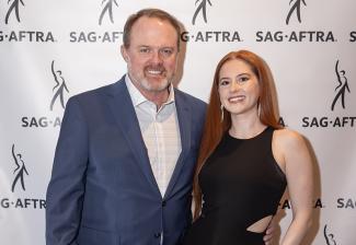 A man in a suit and a woman in a dress stand against a backdrop with SAG-AFTRA  logos.