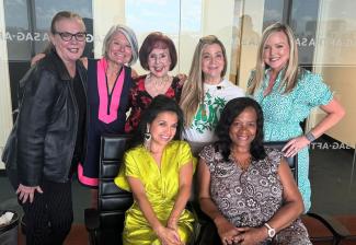 A group of seven women, two seated, five standing, smile while posing in the SAG-AFTRA office.