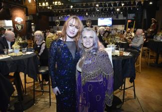 Renee and Aniston stand close, while party-goers sit at tables in the background