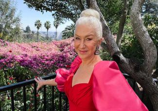 Helen Mirren in red dress with a green foliage background.