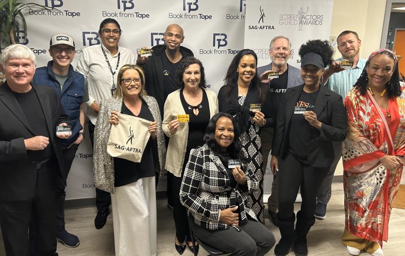 Twelve individuals stand together for a group photo. Bailey, center, kneels close to the ground. Many in the photo show their SAG-AFTRA membership card.