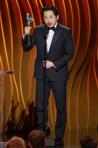 Yeun wears a tuxedo. He holds his statuette with two hands. 