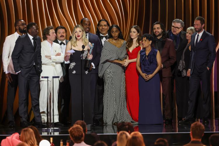 Several individuals stand on stage. 