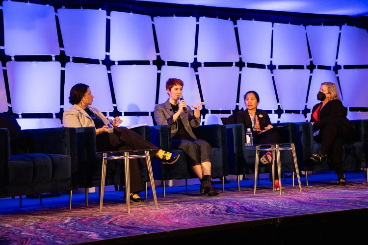 From left, Pathak, Elmaleh, Newman and Reding are seated in chairs. Focus goes to Elmaleh, second from right, who speaks to the audience. 