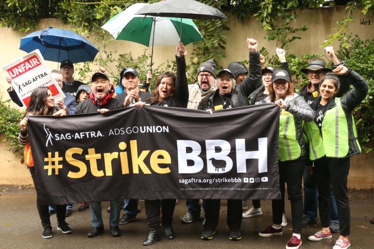 Members holding #StrikeBBH banner in front of a wall with green vines
