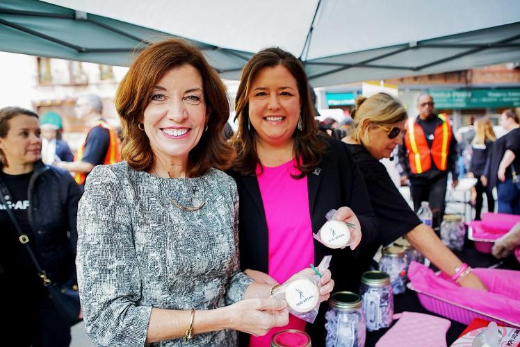 Hochul and Damon hold a cookie with the SAG-AFTRA logo with mason jars of fake money sitting on the table next to them. 