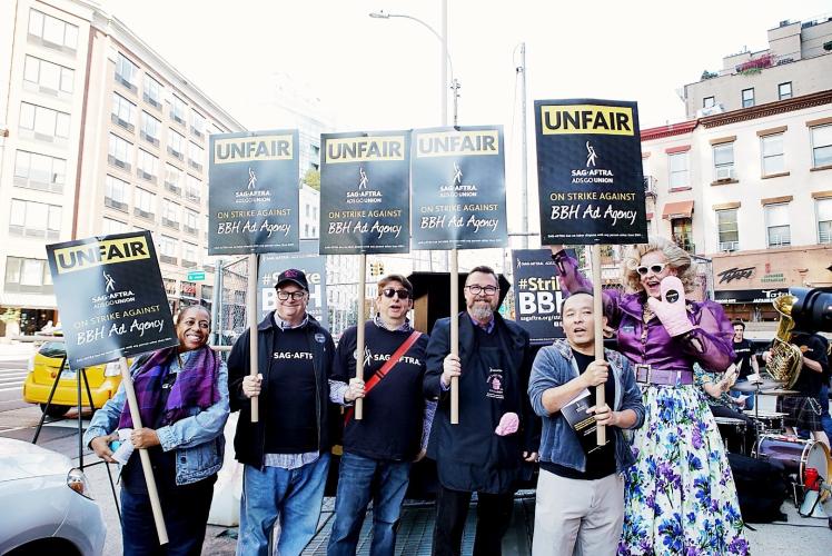 Group photo in front of picket lines outside of BBH office holding strike signs