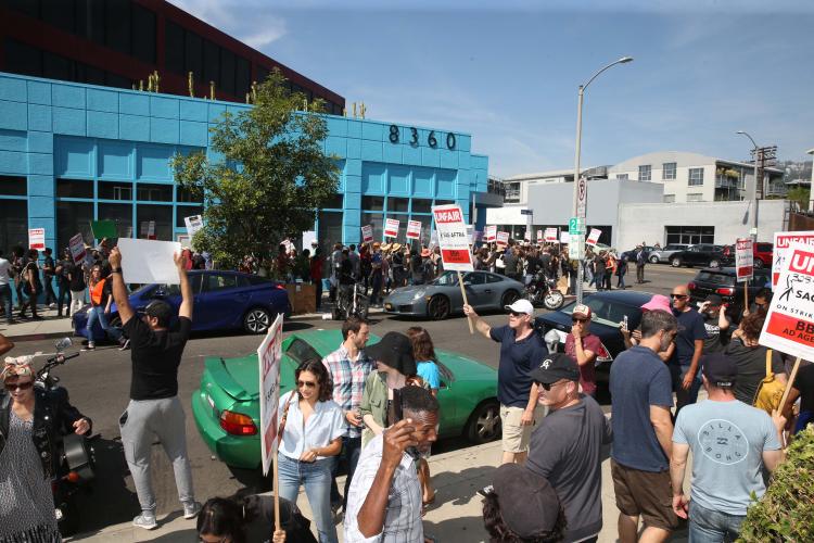 Group of people gathered outside on a street corner holding signs saying "UNFAIR, SAG-AFTRA on strike against BBH Ad Agency"
