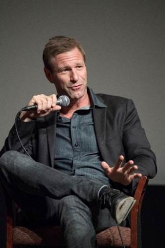 Eckhard in a denim textured button up with a black blazer holding a microphone in his right hand.