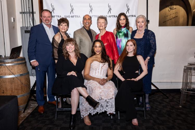 Nine individuals stand in two rows. The six at the top are standing; the three at the bottom are seated. All wear formal attire. Behind them is a white SAG-AFTRA step-and-repeat backdrop.