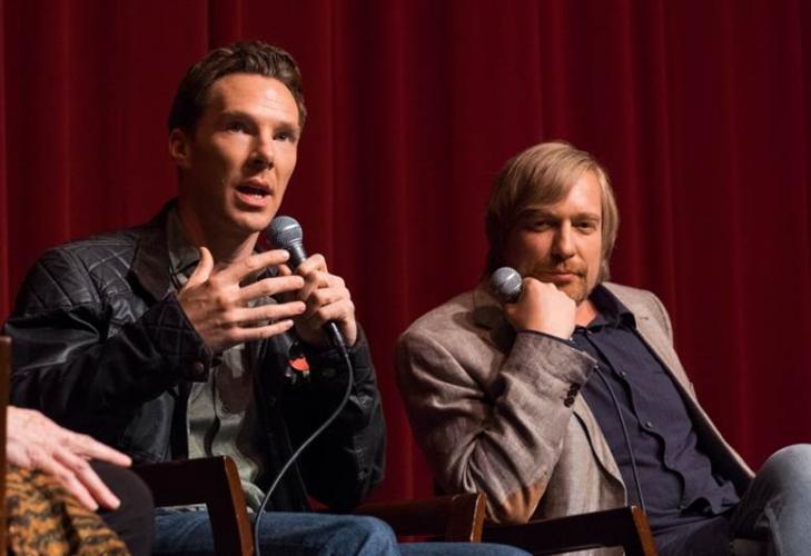Cumberbatch in a black leather jacket speaks into a microphone while Tyldum in a light colored blazer and dark button up listens with his head resting on his fist.