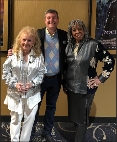 From left, Shutty-MacGregor is in an all-white outfit; Wydra in a suit and argyle-patterned sweater; and Reeves in a black ensemble with yellow flowers. Smiling, they look to the camera.