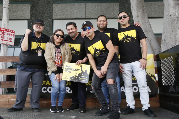 group shot of members standing shoulder to shoulder holding a yellow Fair Contracts poster out front