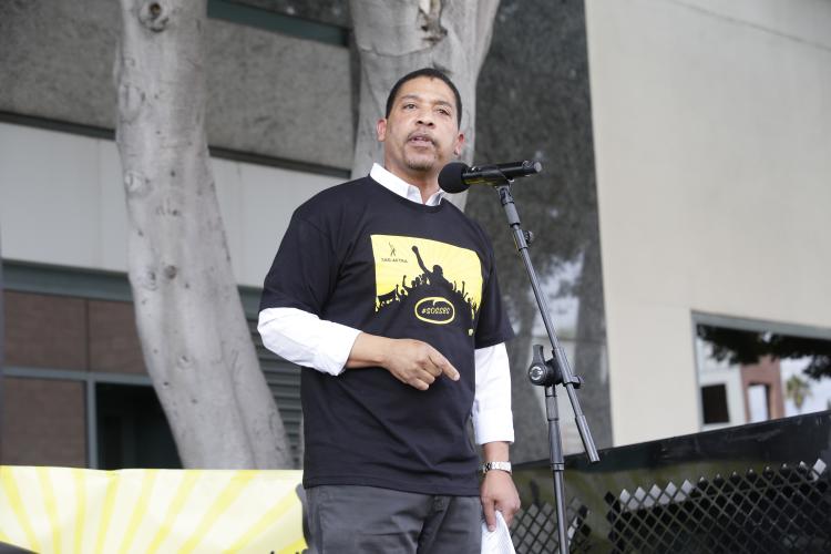 White wearing a black #SOSSBS t-shirt standing at a microphone looking out at the crowd
