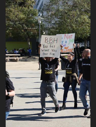Supporter holding up "BBH YOU GET WHAT YOU PAY FOR" sign wearing a black SAG-AFTRA #AdsGoUnion t-shirt.