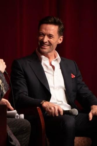 Jackman wearing a white button up and black coat with a red pocket square