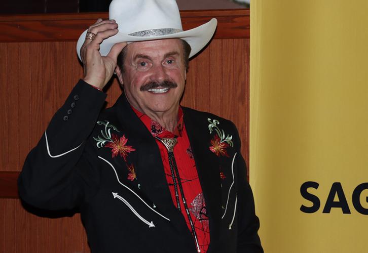 Wolff is dressed in Western garb and is standing next to a yellow SAG-AFTRA banner.
