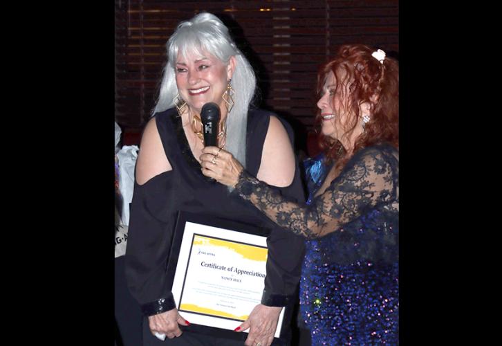 Hall is smiling and holding her certificate while Ghigo holds the mic for her.