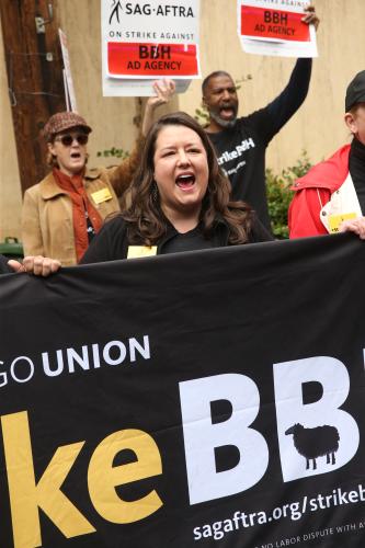 Damon in a black top holds the #StrikeBBH banner in front of her while chanting.