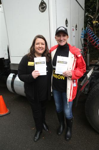 Damon in black long pants and long sleeve shirt and Austin inn black Ads Go Union t-shirt, jeans, black rain boots and an Ads Go Union cap hold a #StrikeBBH flyer in front of them