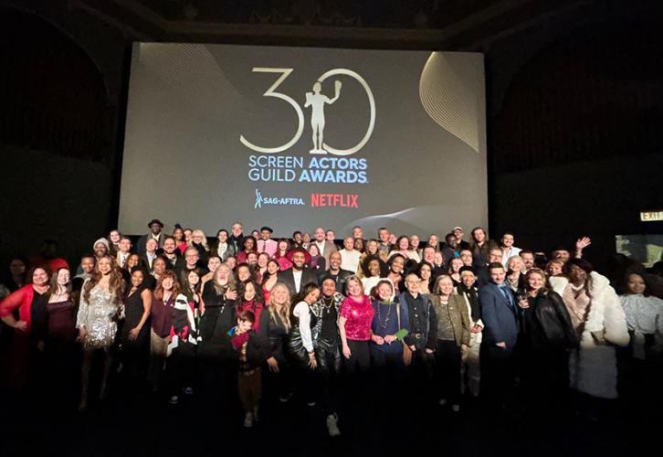 A group of dozens of people pose for a picture under a screen with the SAG Awards logo.