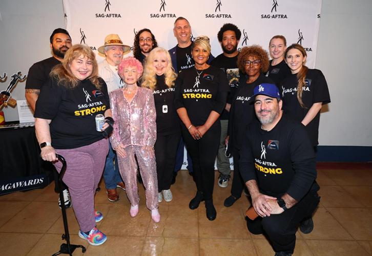 A group of individuals stand in front of a SAG-AFTRA step-and-repeat with a white background and a black SAG-AFTRA logo.