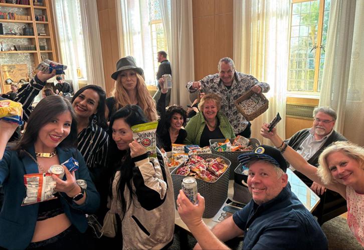A group of people hold snacks in the air around a table.