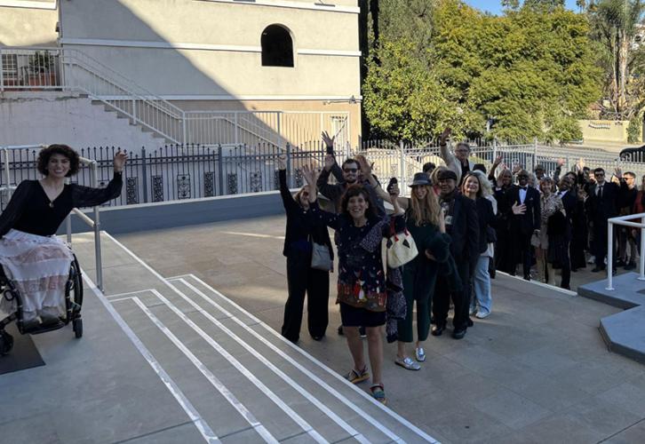 A group of people waving while standing and sitting in a line outside.