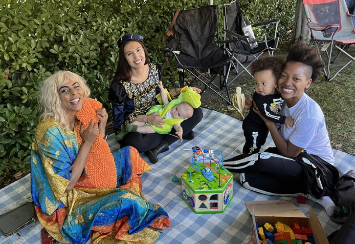 Members and their kids sit on a picnic blanket on the grass.