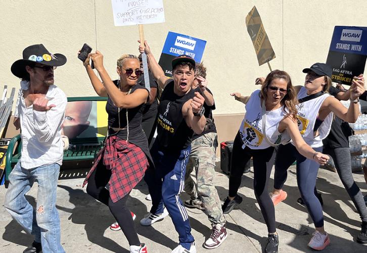 Members dance together while holding picket signs.