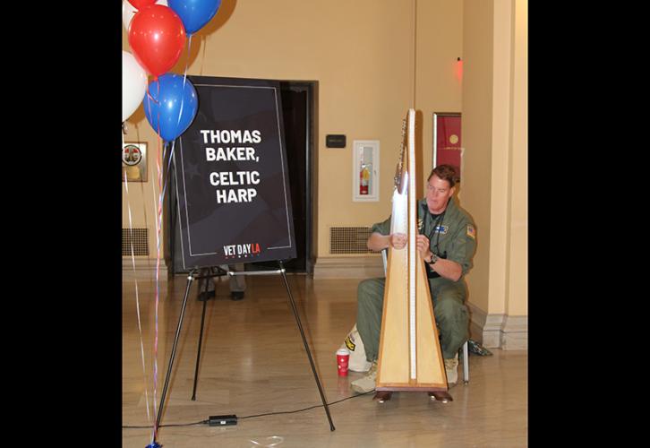 Baker plays his harp next to a sign that says "Thomas Baker, Celtic Harp."